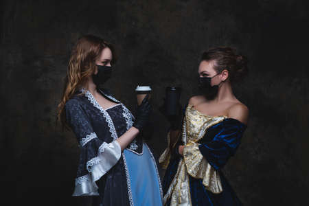 Two women in renaissance dress drinking coffee on abstract dark background, old and new conceptの写真素材