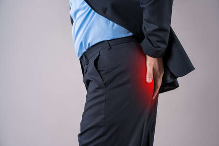 Office worker suffering from hemorrhoids, anal pain on gray background, painful area highlighted in redの写真素材
