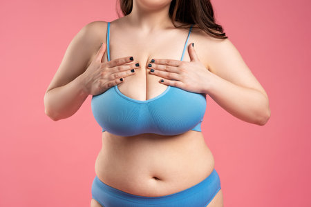 Woman checking her very large breasts for cancer on pink background, health care concept