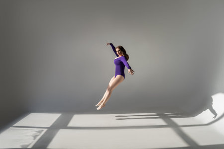 Sexy plus size model with big breasts in purple bodysuit jumping in studio on gray background
