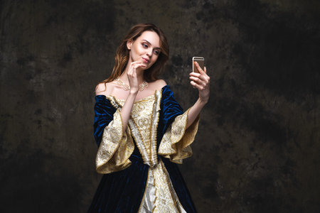 Beautiful woman in renaissance dress taking selfie on smartphone, old and new concept, abstract dark...