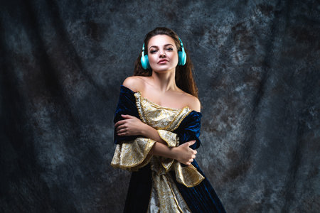 Happy beautiful woman in renaissance dress listens to music in wireless headphones on abstract dark...