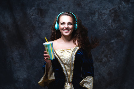 Happy beautiful woman in renaissance dress listens to music in wireless headphones on abstract dark...