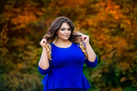 Happy plus size model in blue dress outdoors, fat woman in autumn park among yellow leaves, beauty in natureの写真素材