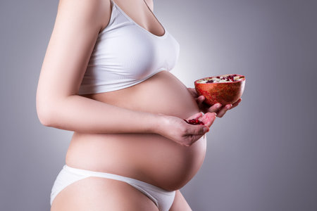 Pregnancy and nutrition - pregnant woman with pomegranate on gray background, vegetarian diet,...