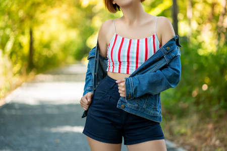 Young fashion model in a top without a bra and a denim jacket on a nature background, modern fashion conceptの写真素材