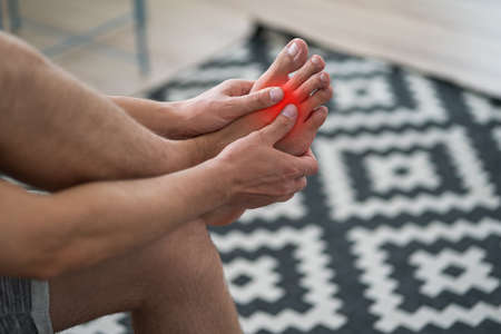 Foot pain, man suffering from feet ache at home, podiatry conceptの写真素材