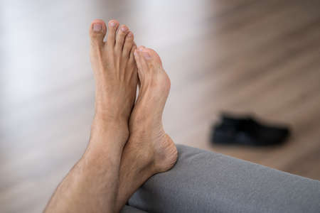 Tired man resting after work at home, male feet, body care concept at home interiorの写真素材