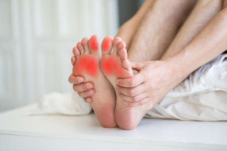 Foot pain, man suffering from feet ache in home interior, podiatry conceptの写真素材