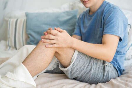 Knee pain, man suffering from ache and doing self-massage at home in bed, self-soothing massagingの写真素材