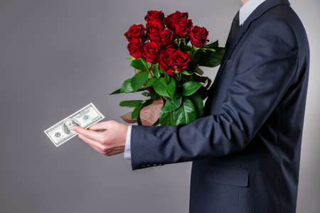 Man with bouquet of red roses and a hundred-dollar bill on a gray background, studio shotの写真素材