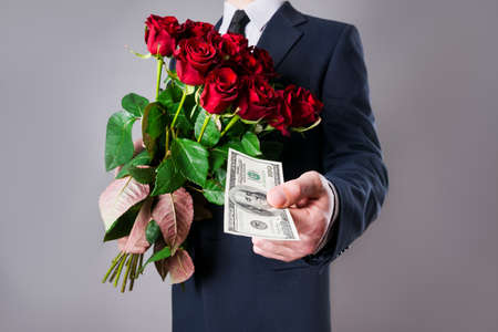 Man with bouquet of red roses and a hundred-dollar bill on a gray background, studio shotの写真素材