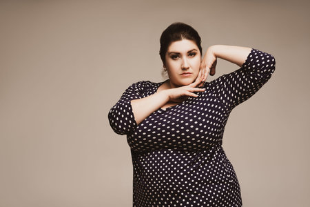 Plus size fashion model in polka dot dress, fat woman on studio background, body positive concept