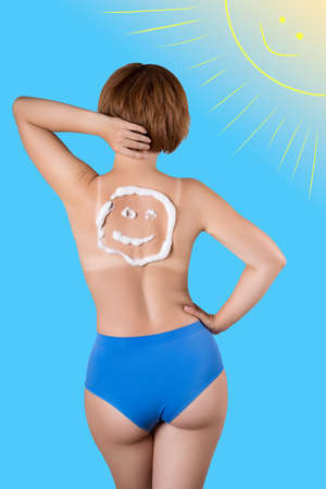 Sunburned woman, sunburn marks on the body, smiley sunscreen on the back, blue background with a painted sunの写真素材