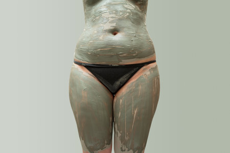 Mud spa procedure, woman applying cosmetic clay body mask, anti cellulite skincare concept, on green backgroundの写真素材