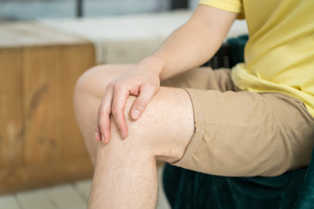 Knee pain, man suffering from ache and doing self-massage at home, self-soothing massagingの写真素材