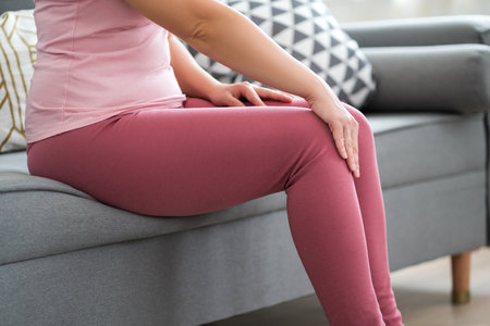 Knee pain, woman suffering from ache and doing self-massage at home, self-soothing massagingの写真素材