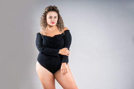 Curvy plus size fashion model in black bodysuit, sexy fat woman in lingerie on gray studio background, body positive conceptの写真素材
