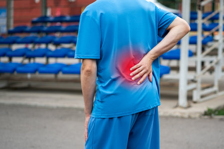 Back pain, kidney inflammation, man suffering from backache on a sports ground after workout, health problems conceptの写真素材