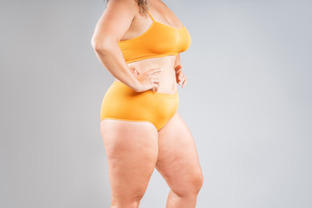 Fat woman in orange underwear on gray studio background, overweight female, body positive conceptの写真素材