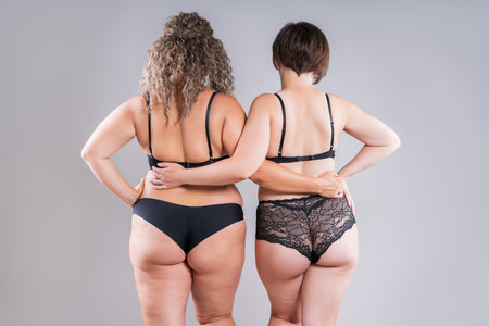 Two overweight women with fat flabby back, hips and buttocks in black lingerie on gray studio background, plastic surgery and body positive conceptの写真素材
