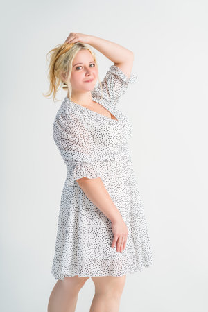 Happy blonde plus size model in polka dot dress, fat woman on gray studio background, body positive conceptの写真素材