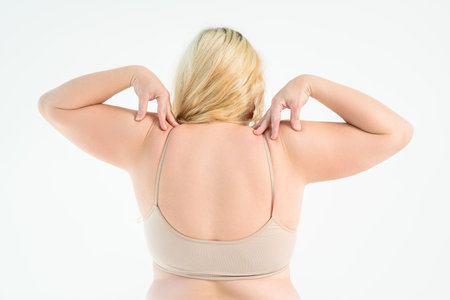 Overweight woman with fat back rubbed her shoulders with bra straps, obesity female body on white studio backgroundの写真素材