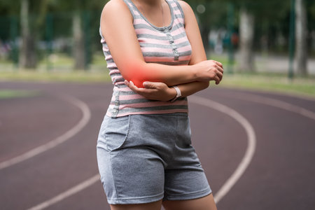 Diseases of the elbow joint, bone fracture and inflammation, tendon injury, athletic woman on a running track after workout suffering from pain in her hand, healthy lifestyle conceptの写真素材