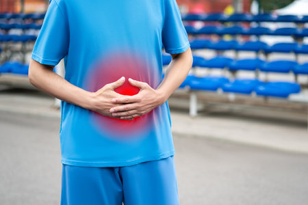 Athletic man with stomach ache on a sports ground after workout, health problems conceptの写真素材