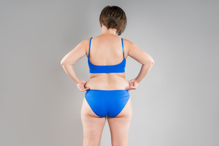 Overweight woman with fat back, hips and buttocks, obesity female body on gray background, studio shotの写真素材