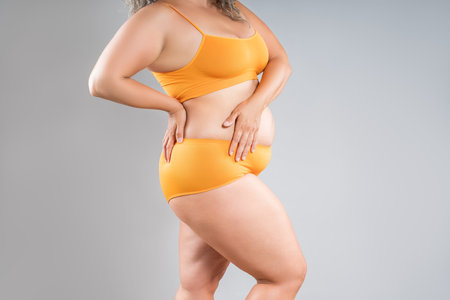Fat woman in orange underwear on gray studio background, obesity and cellulite, overweight female body, weight loss conceptの写真素材