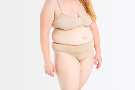 Fat woman in beige underwear on gray studio background, overweight female body, plastic surgery conceptの写真素材