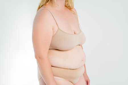 Fat woman in beige underwear on gray studio background, overweight female body, plastic surgery conceptの写真素材
