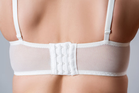 Woman properly wearing fitting bra, close-up female back in a white brassiere on gray studio backgroundの写真素材