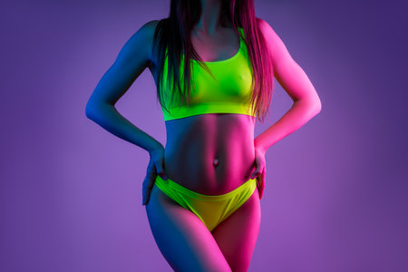 Muscular sexy fitness woman in green lingerie on purple studio background, neon lightの写真素材