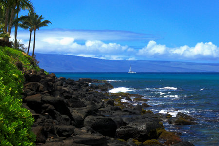 A sailboat off the rocky coast of Maui, Hawaii with the Island of Lanai in the backgroundの写真素材
