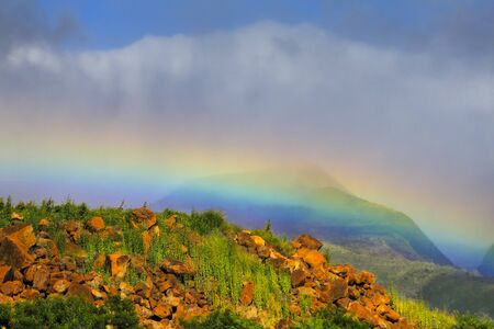 A bright horizontal rainbow just above the horizon with a mountain backdrop in Maui, Hawaiiの写真素材