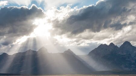 Rays of sunlight break through the clouds onto the Grand Teton Mountain Range in Grand Teton National Parkの写真素材