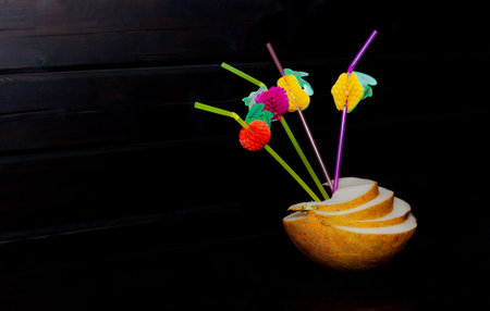 sliced â€‹â€‹melon with inserted multi-colored straws on a black background. Summer...