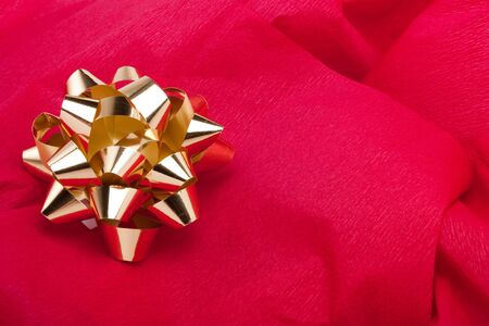 Gold Christmas bow decoration on red crepe paper backgroundの写真素材