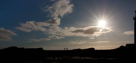 Silhouette of couple on rocks next to Southerness Point Lighthouse, Solway Firth, Dumfries and Galloway,South West Coast of Scotland.の写真素材