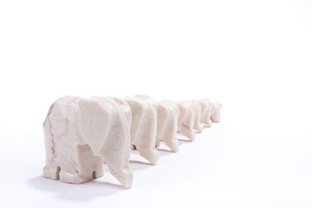 A line of seven marble elephant ornaments isolated against white background.の写真素材