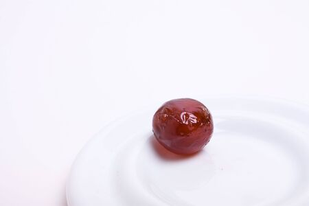 A pitted dark glossy Morello Glace cherry on white plate against white background.の写真素材