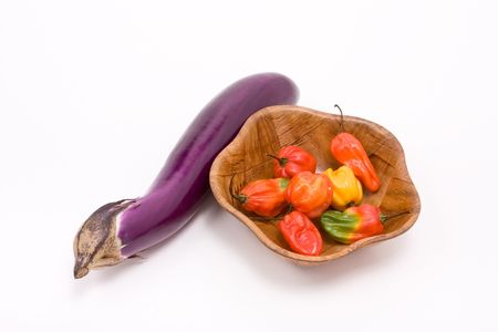 Mixed Caribbean scotch bonnet Chillies in wooden bowl with shiny aubergine against white backgroundの写真素材
