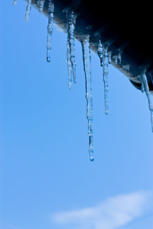 Close up abstract of Icicles hanging from roof of building against blue sky and snow.