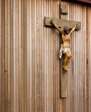 Statue figure of Jesus crucified on wooden cross against wooden panneled wall.の写真素材