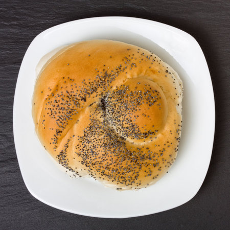 Seeded bread roll on white plate from high viewpoint against dark slate  background.の写真素材