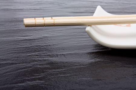 Pair of wood or bamboo Chopsticks in wrapper arranged on rest against dark slate background.の写真素材