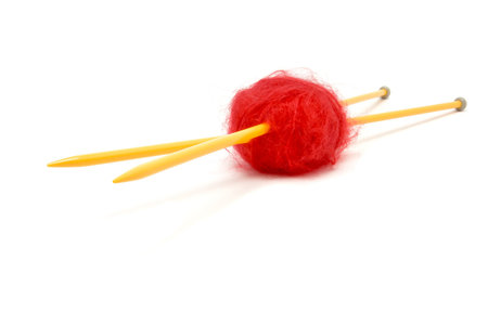 A small ball of red mohair wool pierced with large yellow knitting kneedles against white.