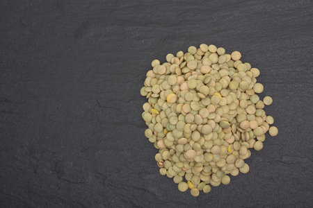 Pile of Green lentils on dark slate background .